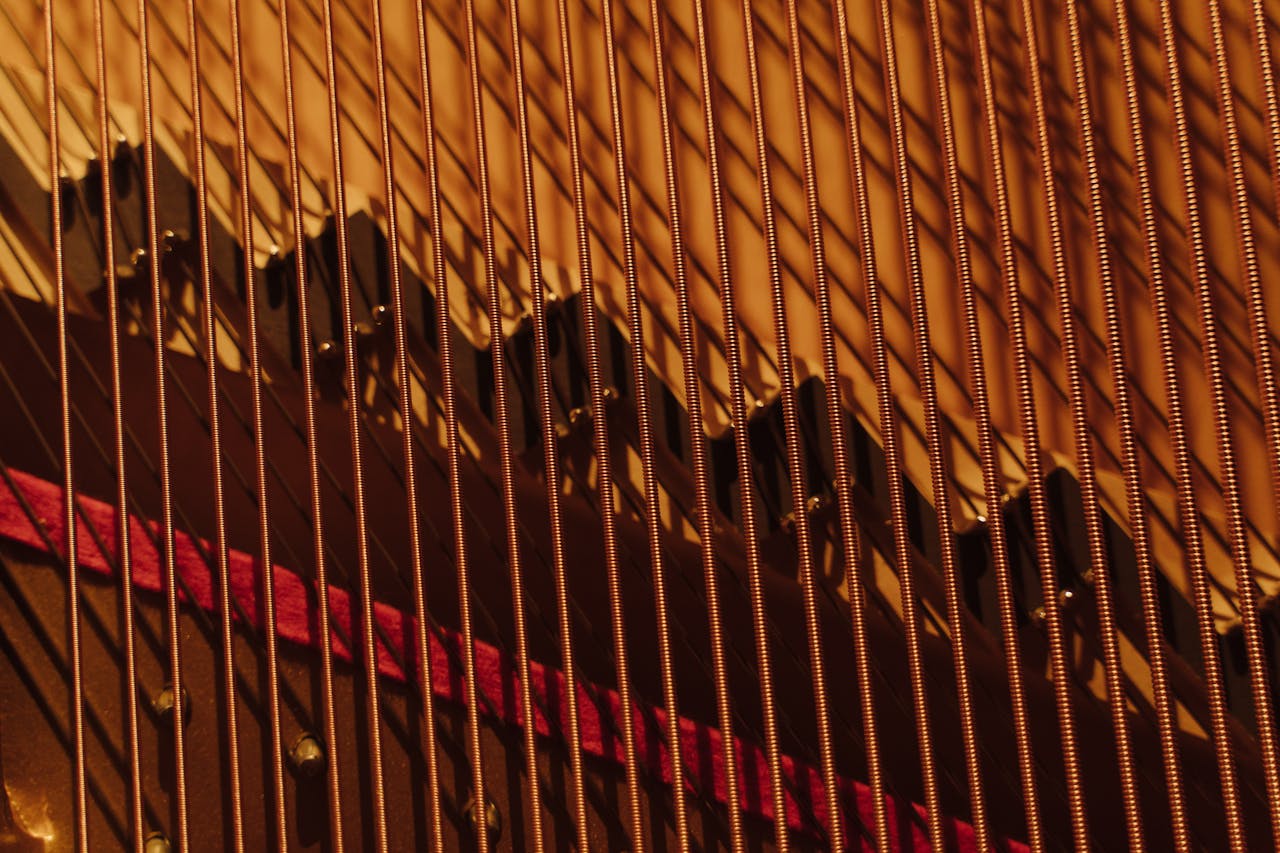 Detailed view of piano strings under warm lighting, showcasing intricate details and metallic textures.